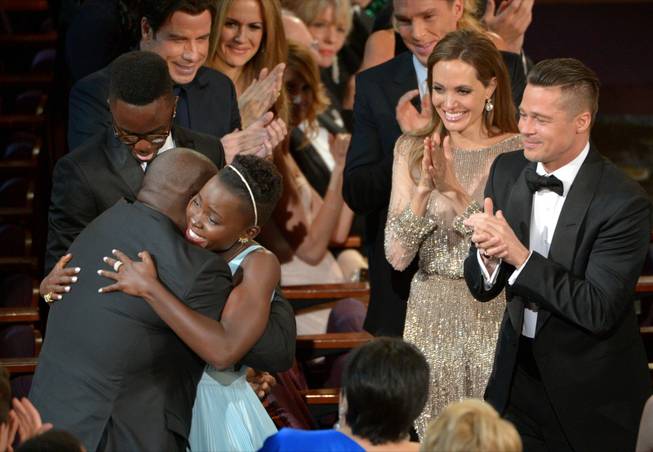 Director Steve McQueen, left, congratulates Lupita Nyong'o on her win for best actress in a supporting role for "12 Years a Slave" as her brother Peter, background from left, and actors John Travolta, Kelly Preston, Benedict Cumberbatch, Angelina Jolie and Brad Pitt, look on, during the Oscars at the Dolby Theatre on Sunday, March 2, 2014, in Los Angeles. (Photo by John Shearer/Invision/AP)
