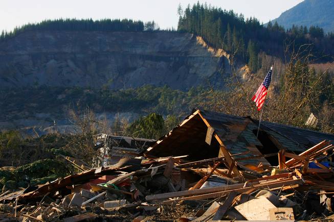 A flag sits atop what was Cory Kuntz and family's home Sunday, March 23, 2014. The family was at a baseball game Saturday morning when the fatal mudslide swept through the area, destroying everything on their property. The area where the land broke away is seen in the background.