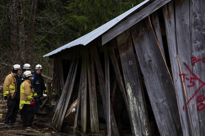 Search and rescue workers assess a damaged structure and what needed to be done to stabilize it before entering into it, in the debris field caused by the massive mudslide above the North Fork of the Stillaguamish River onto Highway 530, as recovery efforts are underway, near Oso, Wash., on Tuesday, March 25, 2014.