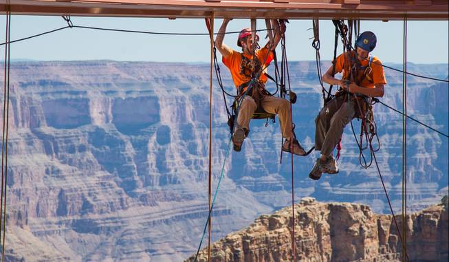 In this Tuesday, March, 25, 2014, photo provided by Abseilon USA via AZ Photos, technicians dangle from a series of ropes before polishing the underside glass at Grand Canyon Skywalk in Hualapai Reservation, Ariz. The more than 40 panes of glass underneath the horseshoe-shaped bridge on the Hualapai reservation aren’t easily accessible. The structure juts out 70 feet from the edge of the Grand Canyon, offering visitors a view of the Colorado River 4,000 feet below.