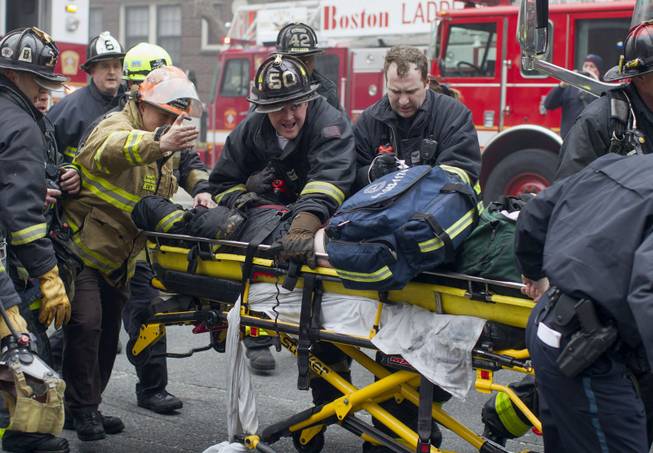 Firefighters and emergency medical personnel rush a firefighter from the scene of a multi-alarm fire at a four-story brownstone in the Back Bay neighborhood near the Charles River, Wednesday, March 26, 2014, in Boston. Boston EMS spokesman Nick Martin says four people, including at least three firefighters, have been taken to hospitals.