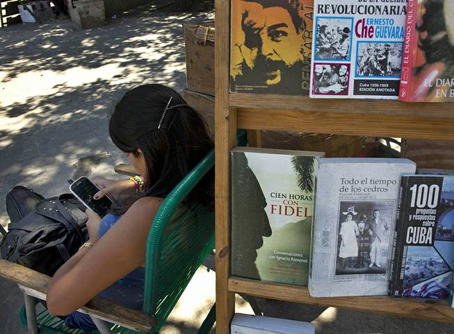 A book street vendor passes the time on her smart phone as she waits for customers in Havana, Cuba, Tuesday, April 1, 2014. The Obama administration secretly financed a social network in Cuba to stir political unrest and undermine the country’s communist government, according to an Associated Press investigation.