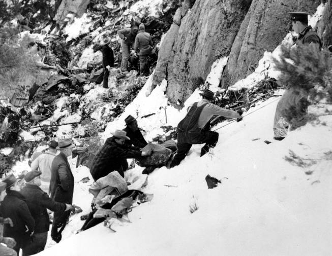 The blanket-wrapped body of film actress Carole Lombard is removed from the shattered wreckage of the Los Angeles bound TWA air liner on Table Mountain, near Las Vegas, Nev., on Jan. 18, 1942. Lombard, 33, who was on tour to sell war bonds, and 21 other passengers, were killed when the plane crashed into the cliff high on the snow-covered mountain on Jan. 16. In the background are searchers looking for other bodies.