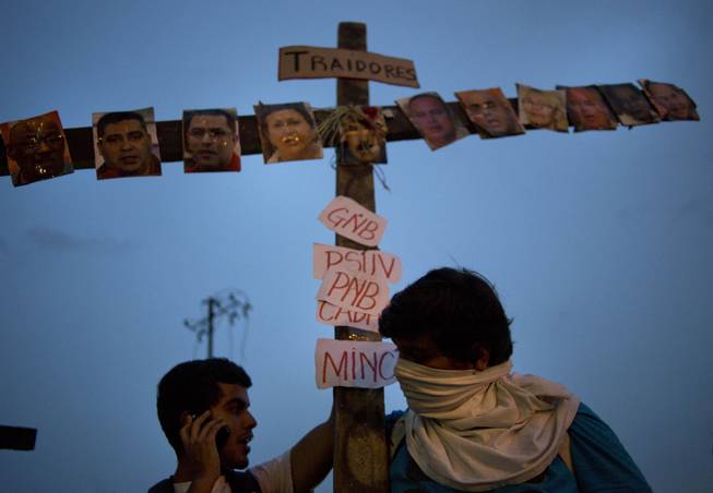 Anti-government protesters carry a cross covered with photos of government officials and supporters under the Spanish word "Traitors" at a demonstration during Holy Week in Caracas, Venezuela, Wednesday, April 16, 2014. The opposition wants President Nicolas Maduro's government to free jailed opponents and create an independent truth commission to determine responsibility for deaths tied to protests that have rocked the nation since February.