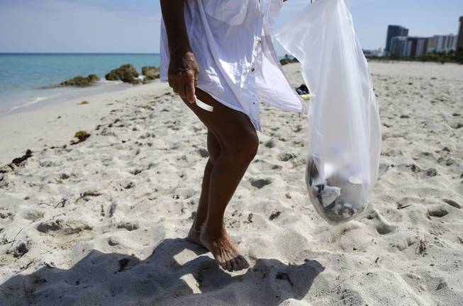 Herminia Hernandez gathers trash on the beach while volunteering to pick up trash on Earth Day, Tuesday, April 22, 2014, in Miami Beach, Fla. People across the globe held events on Earth Day to celebrate the earth's environment and spread awareness on how to conserve its natural resources.