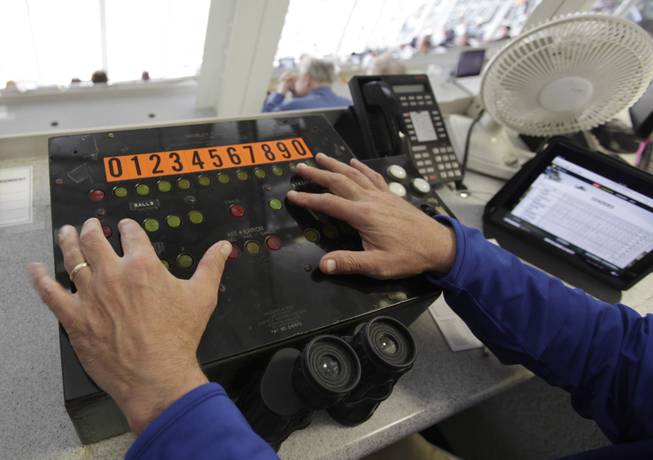 In this April 10, 2014 photo, Rick Fuhs operates a panel full of buttons in the press box behind home plate that sends an electrical charge into a panel of half ball-shaped itargets,i causing specific ones to flip so that they add up to form the number of the batter, and the number of balls, strikes and outs on Wrigley Field's iconic scoreboard during a baseball game between Pittsburgh Pirates and Chicago Cubs, in Chicago. This switch box and the only electronically operated part of the display on Wrigley Field's iconic scoreboard were built in 1937 and still being used at the ballpark.