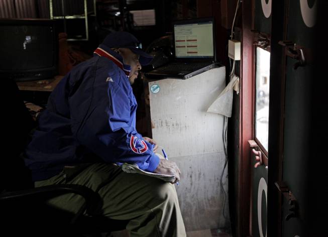 In this April 10, 2014, photo, scoreboard operator Darryl Wilson looks out to the field from inside Wrigley Field's iconic scoreboard during a baseball game between the Pittsburgh Pirates and the Chicago Cubs. Wilson mans the two top floors, little more than scaffolding of the three-level scoreboard, tracking scores from around baseball and changing scores and the uniform numbers of pitchers as managers in those games bring in relievers.