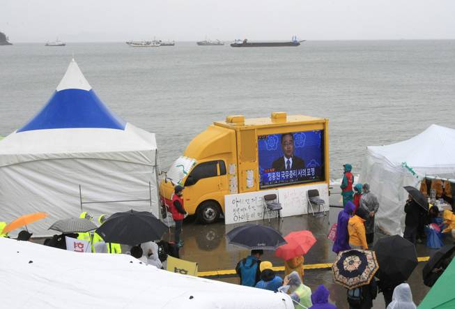 Relatives of passengers aboard the sunken ferry Sewol and onlookers watch a televsion news program showing South Korean Prime Minister Chung Hong-won offering his resignation at a port in Jindo, South Korea, Sunday, April 27, 2014. Chung offered to resign Sunday over the government's handling of the deadly ferry sinking, blaming "deep-rooted evils" and irregularities in a society for a tragedy that has left more than 300 people dead or missing and led to widespread shame, fury and finger-pointing.
