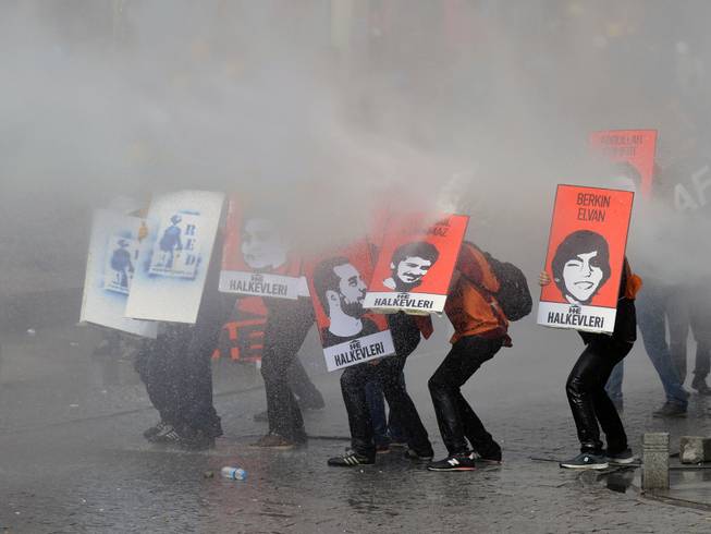 Protesters hold posters with images of the victims of the last year's protests as riot police use water cannons and teargas to disperse thousands of people trying to reach the city's main Taksim Square to celebrate May Day in Istanbul, Turkey, Thursday, May 1, 2014. Clashes erupted between May Day demonstrators and riot police as crowds determined to defy a government ban tried to march to the city's iconic Taksim Square. Security forces pushed back demonstrators with water cannons and tear gas.