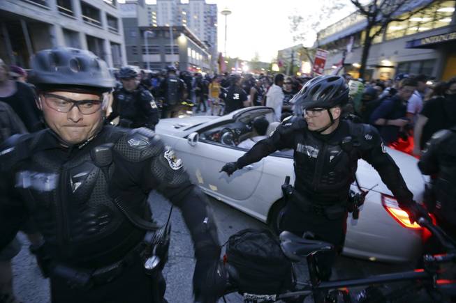 A car makes its way through protesters and police during May Day activities Thursday, May 1, 2014 in Seattle. Police have made several arrests and fired pepper spray as anti-capitalist marchers meandered through Seattle several hours after hundreds of peaceful demonstrators took part in a May Day march in support of immigrant rights and a boost in the minimum wage.