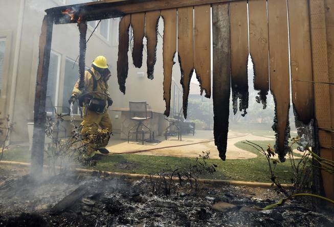 A Firefighter puts water on a house fence during a wildfire Wednesday, May 14, 2014, in Carlsbad, Calif. More wildfires broke out Wednesday in San Diego County threatening homes in Carlsbad and forcing the evacuations of military housing and an elementary school at Camp Pendleton as Southern California is in the grip of a heat wave. (AP Photo)