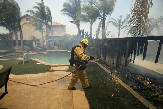 A Firefighter puts water on a house fence during a wildfire Wednesday, May 14, 2014, in Carlsbad, Calif. More wildfires broke out Wednesday in San Diego County threatening homes in Carlsbad and forcing the evacuations of military housing and an elementary school at Camp Pendleton as Southern California is in the grip of a heat wave.