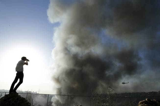 Travis Lowell takes a picture as smoke from wildfires rise, Wednesday, May 14, 2014, in Carlsbad, Calif. More wildfires broke out Wednesday in San Diego County threatening homes in Carlsbad and forcing the evacuations of military housing and an elementary school at Camp Pendleton as Southern California is in the grip of a heat wave. (AP Photo)