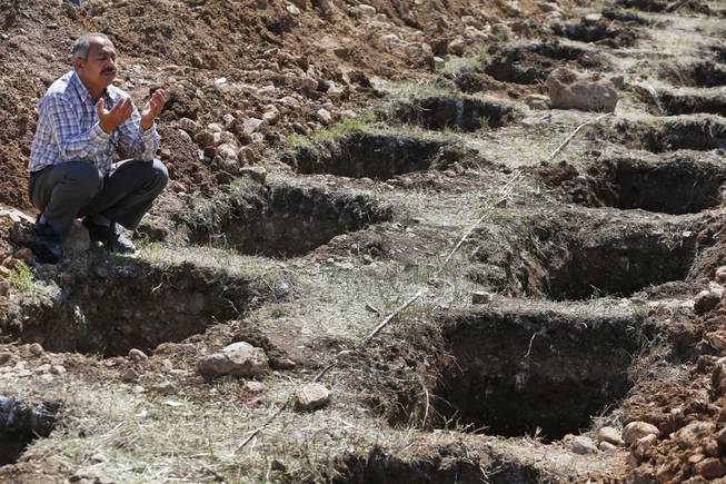 A man offers his prayers for the victims of the mining accident being buried during their funeral procession as he sits by empty graves prepared for the victims, in Soma, Turkey, Thursday, May 15, 2014. An explosion and fire at a coal mine in Soma, some 250 kilometers (155 miles) south of Istanbul, killed hundreds of workers, authorities said, in one of the worst mining disasters in Turkish history.