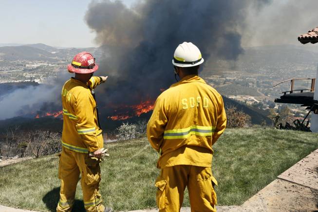 Firefighters plan their attack as the brush fire flares up heading toward homes Thursday, May 15, 2014, in San Marcos, Calif. Gusty winds failed to return Thursday morning in San Diego County wildfire areas and authorities said it was a window of opportunity to make further gains against flames that burned homes and drove tens of thousands from their homes.