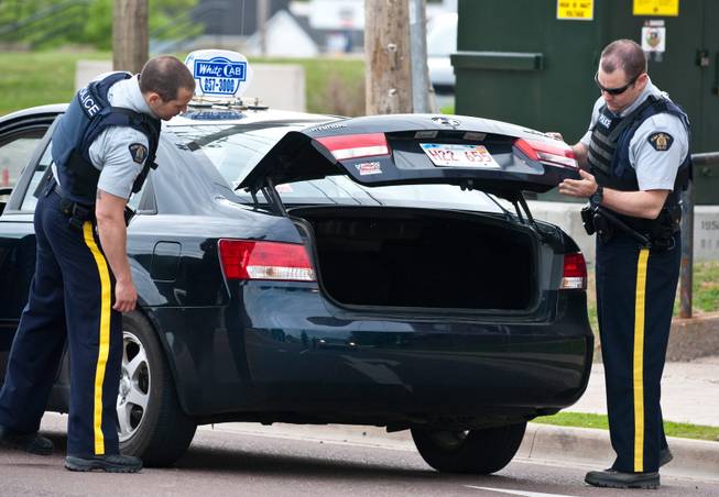 Royal Canadian Mounted Police check the trunk of a taxi at a roadblock in Moncton, New Brunswick on Thursday, June 5, 2014. A RCMP manhunt for a gunman suspected of killing three Mounties and wounding two others passed the 12-hour mark Thursday in Moncton as a large section of the New Brunswick city was under a virtual siege.