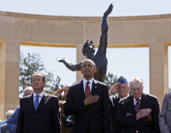 U.S. President Barack Obama, center, and French President Francois Hollande, left, stand with veterans during the playing of Taps at Normandy American Cemetery at Omaha Beach as he participates in the 70th anniversary of D-Day in Colleville sur Mer, Normandy, France, Friday, June 6, 2014.