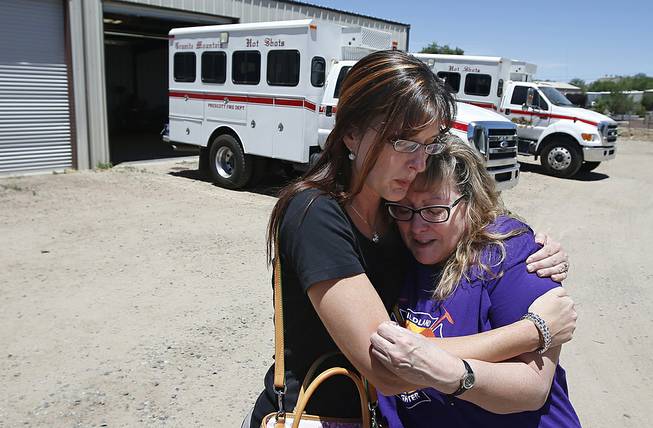 In this Tuesday, June 24, 2014 photo, in her first visit to the firehouse in Prescott, Ariz., since her son's death, Colleen Turbyfill, right, Travis Turbyfill's mother, gets a hug from Katie Cornelius, Prescott Fire Department volunteer exhibit curator for the Tribute Fence Preservation Project, after Turbyfill visited the Granite Mountain Hotshots crew vehicle buggy where her son Travis sat before he was killed along with 18 other hotshots in a wildfire almost a year ago.