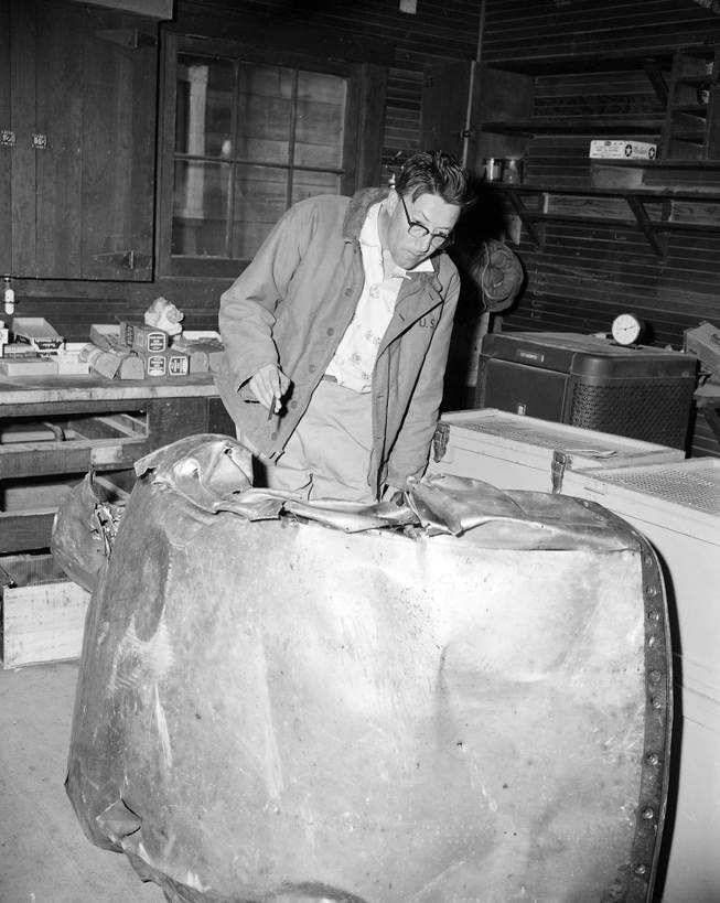 FILE - In this July 5, 1956 file photo, reporter Al Thrasher inspects the wreckage of a United Airlines UAL DC-7, which collided into a TWA Constellation on June 30, 1956, killing all 128 persons on board both planes, after it was brought out of the Grand Canyon. On Tuesday, July 8, 2014, the Grand Canyon National Park will mark the designation of the crash site as a National Historic Landmark in a ceremony overlooking the gorge where the wreckage was scattered over 1.5 square miles.