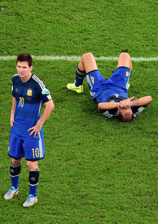 Argentina's Pablo Zabaleta lies on the pitch as Lionel Messi stands beside him after the World Cup final soccer match between Germany and Argentina at the Maracana Stadium in Rio de Janeiro, Brazil, Sunday, July 13, 2014. Mario Goetze volleyed in the winning goal in extra time to give Germany its fourth World Cup title with a 1-0 victory over Argentina on Sunday.