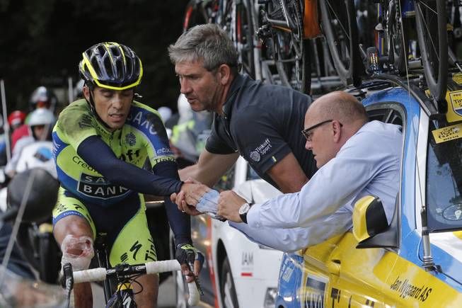 Spain's Alberto Contador gets assistance from his team after crashing during the tenth stage of the Tour de France cycling race over 161.5 kilometers (100.4 miles) with start in Mulhouse and finish in La Planche des Belles Filles, France, Monday, July 14, 2014. Contador withdrew from the race as a result of the crash, right is his team manager Bjarne Riis of Denmark.