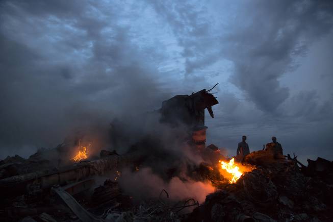 File - This July 17, 2014, file photo show people walking amongst the debris at the crash site of Malaysia Airlines Flight 17 near the village of Hrabove, eastern Ukraine. Ukraine said the passenger plane was shot down as it flew over the country, killing all 298 people on board. Aviation has suffered one of its worst weeks in memory, a cluster of disasters spanning three continents.