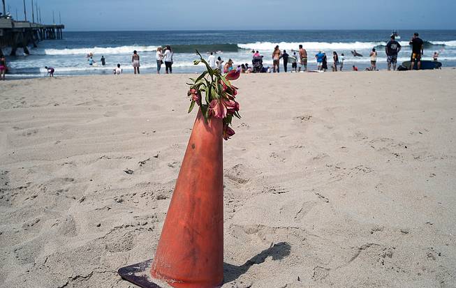 A bouquet of flowers is set on a warning cone at the Venice Beach pier in Los Angeles, Monday, July 28, 2014. Los Angeles' popular Venice Beach teemed with people enjoying a weekend outing on the boardwalk and sand when lifeguards and other witnesses say lightning from a rare summer thunderstorm hit without warning, injuring or rattling more than a dozen people and leaving a 21-year-old man dead.