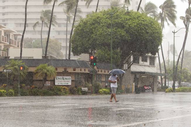 A man uses an umbrella against the rain as he walks across Kapiolani Blvd in Waikiki in Honolulu on Friday, Aug. 8, 2014. Rain and wind gusts are hitting parts of Oahu as Tropical Storm Iselle heads towards the island. Iselle is the first tropical storm to hit the state in 22 years.