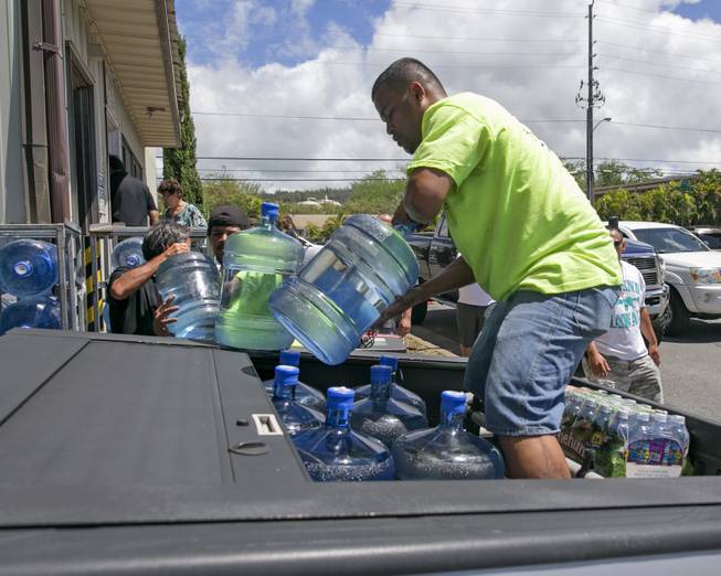 Workers at the Menehune Water Company load five gallon bottles of water into a customer's truck, Thursday, Aug. 7, 2014, in Aiea, Hawaii. Hawaii is bracing for two back to back hurricanes, Iselle and Julio, which are on course to hit the Islands. Bottles of water are quickly disappearing off shelves in Hawaii causing many people to line up for several hours to purchase water directly from the company.