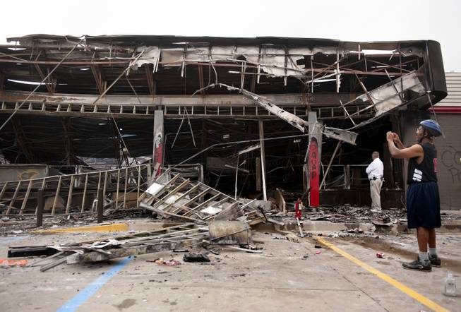 Passers-by and media take a closer look Monday, Aug. 11, 2014 at the burned-out shell of the QuikTrip gas station torched during the violence that erupted in Ferguson, Mo. overnight following a candle-light memorial for 18-year-old shooting victim Michael Brown. Police said Brown, who was unarmed, was fatally shot Saturday in a scuffle with an officer.