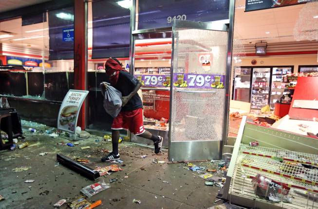 A man leaves a store on Sunday, Aug. 10, 2014, in Ferguson, Mo. A few thousand people crammed a suburban St. Louis street Sunday night at a vigil for unarmed 18-year-old Michael Brown who was shot and killed by a police officer, while afterward several car windows were smashed and stores were looted as people carried away armloads of goods as witnessed by an an Associated Press reporter.