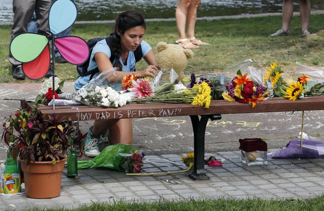 Mariagrazia LaFauci, 24, of Waltham, Mass. places a teddy bear on a bench at Boston's Public Garden, Tuesday, Aug. 12, 2014, where a small memorial has sprung up at the place where Robin Williams filmed a scene during the movie, "Good Will Hunting." Williams, 63, died at his San Francisco Bay Area home Monday in an apparent suicide.