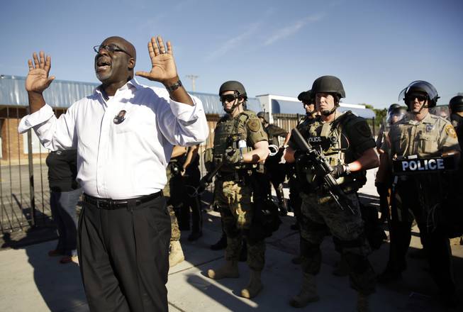 A community activist tries to persuade a group of protesters to move back as police in riot gear watch protesters in Ferguson, Mo. on Wednesday, Aug. 13, 2014. On Saturday, Aug. 9, 2014, a white police officer fatally shot Michael Brown, an unarmed black teenager, in the St. Louis suburb.
