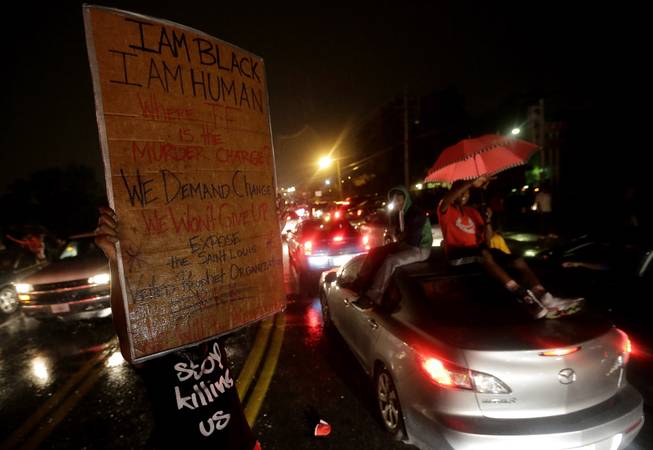 A protester holds up a sign Friday, Aug. 15, 2014, in front of a convenience store that was looted and burned following the shooting death of Michael Brown by police nearly a week ago in Ferguson, Mo. A suburban St. Louis police chief on Friday identified the officer whose fatal shooting ignited days of heated protests, and released documents alleging the teen was killed after a robbery in which he was suspected of stealing a box of cigars.