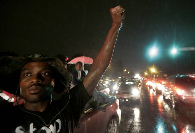 A protester holds up a clenched fist Friday, Aug. 15, 2014, in front of a convenience store that was looted and burned following the shooting death of Michael Brown by police nearly a week ago in Ferguson, Mo. A suburban St. Louis police chief on Friday identified the officer whose fatal shooting ignited days of heated protests, and released documents alleging the teen was killed after a robbery in which he was suspected of stealing a box of cigars.