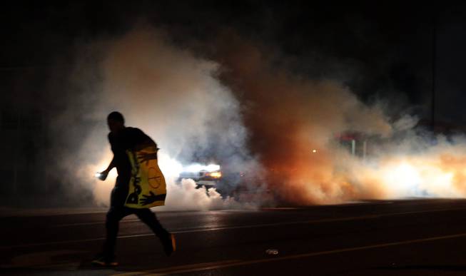 A protestor runs down the street to escape tear gas fired at demonstrators on Sunday, Aug. 17, 2014, in Ferguson, Mo. As night fell Sunday in Ferguson, another peaceful protest quickly deteriorated after marchers pushed toward one end of a street. Police attempted to push them back by firing tear gas and shouting over a bullhorn that the protest was no longer peaceful.