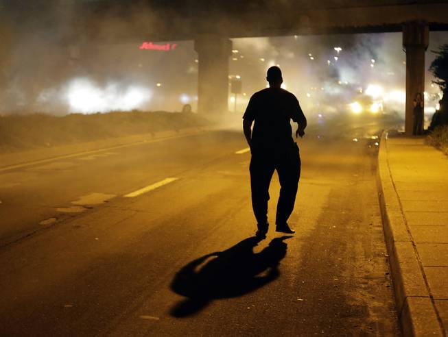 A man walks in the street after police fired tear gas to disperse a crowd Sunday, Aug. 17, 2014, during a protest for Michael Brown, who was killed by a police officer last Saturday in Ferguson, Mo. As night fell Sunday in Ferguson, another peaceful protest quickly deteriorated after marchers pushed toward one end of a street. Police attempted to push them back by firing tear gas and shouting over a bullhorn that the protest was no longer peaceful.