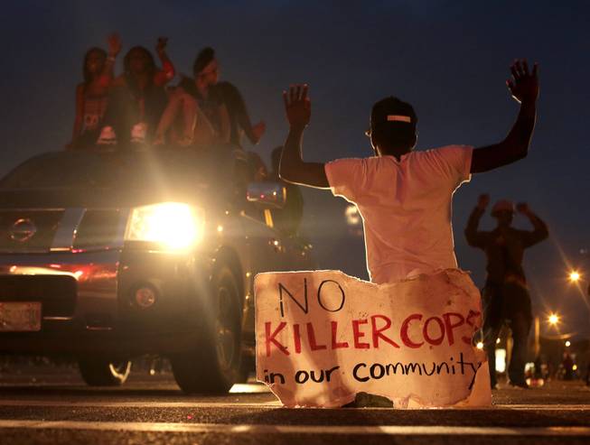 People protest Sunday, Aug. 17, 2014, for Michael Brown, who was killed by a police officer last Saturday in Ferguson, Mo. As night fell Sunday in Ferguson, another peaceful protest quickly deteriorated after marchers pushed toward one end of a street. Police attempted to push them back by firing tear gas and shouting over a bullhorn that the protest was no longer peaceful.