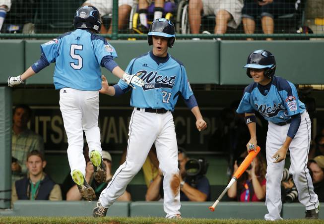 Las Vegas' Justin Hausner (5) leaps on home plate and celebrates with teammates Austin Kryszczuk (21) and Brad Stone, right, after all three runs scored on a double by Drew Laspaluto off Chicago's Joshua Houston in the first inning of a United States Championship game at the Little League World Series in South Williamsport, Pa., Saturday, Aug. 23, 2014. (AP Photo/Gene J. Puskar