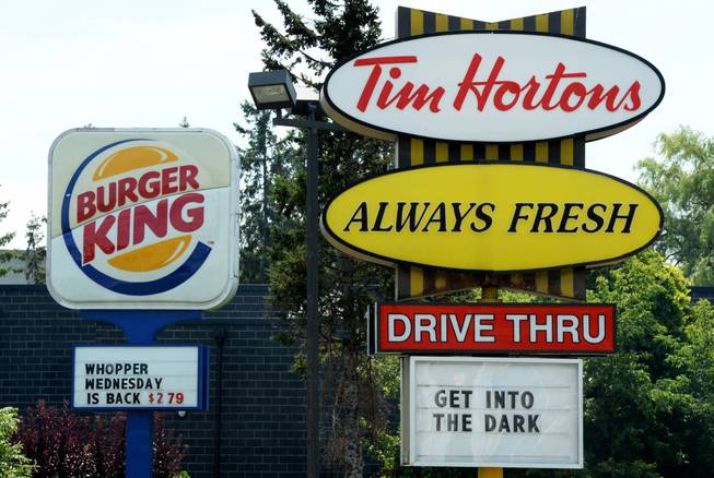 A Burger King sign and a Tim Hortons sign are displayed on St. Laurent Boulevard in Ottawa, Canada, on Monday, Aug. 25, 2014. Canada's iconic coffee chain, Tim Hortons, and Miami-based Burger King say they will join forces, but will operate as independent brands to form the world's third-largest quick service restaurant company.