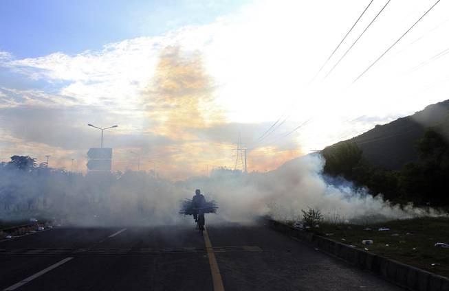 A bicyclist makes his way through tear gas fired by police to disperse protesters, carrying wood for cooking as the sun sets, in Islamabad, Pakistan, Monday, Sept. 1, 2014. Anti-government protesters stormed Pakistan’s state television building Monday, forcing the channel briefly off the air as they clashed with police and pushed closer to the prime minister’s residence. The violence comes as part of the mass demonstrations led by cleric Tahir-ul-Qadri and opposition politician Imran Khan that demand Prime Minister Nawaz Sharif resign.