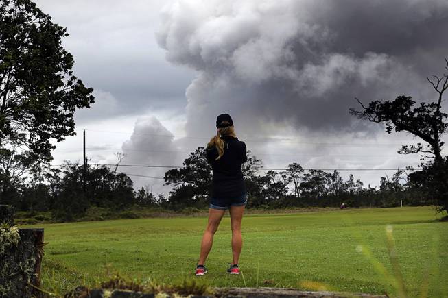 Marie Brant, of Laguna Niguel, Calif., watches as ash rises from the summit crater of Kilauea volcano, Thursday, May 17, 2018, in Volcano, Hawaii. Brant is on vacation in Hawaii. The volcano on Hawaii's Big Island erupted anew Thursday shortly after 4 a.m. with little sound and only modest fury, spewing a steely gray plume of ash about 30,000 feet into the sky that began raining down on a nearby town.