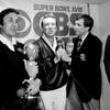 In this Jan. 23, 1984, file photo, Oakland Raiders coach Tom Flores clutches the Super Bowl trophy as Raiders managing general partner Al Davis is interviewed by Brent Musburger in the locker room after their 38-9 win over the Washington Redskins in Super Bowl XVIII in Tampa, Fla. At right is NFL Commissioner Pete Rozelle.